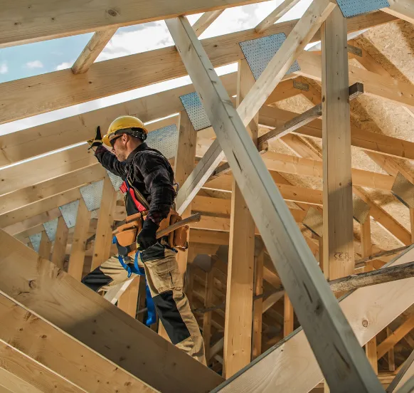 Construction worker installing a wooden roof truss system under a blue sky, representing residential framing and roofing projects in Los Angeles.